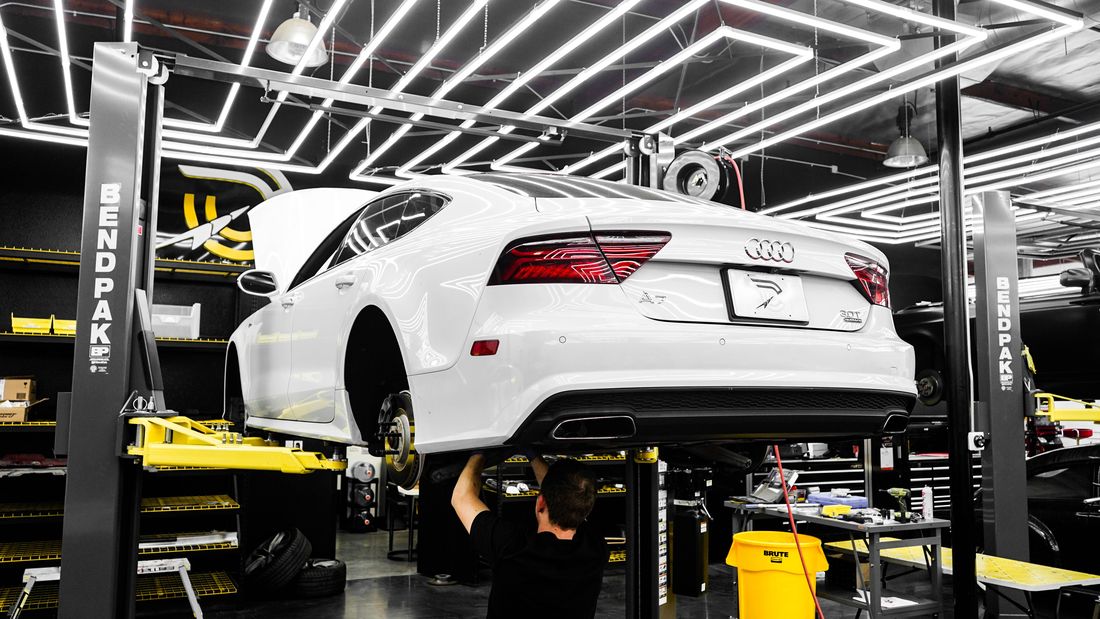 A saloon car raised on a two post lift under the workshop light rig